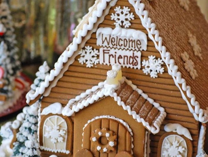 une maison en pain d épices heut de gamme décorée avec des petits bonhommes de gingembre devant la porte sapins decoratifs