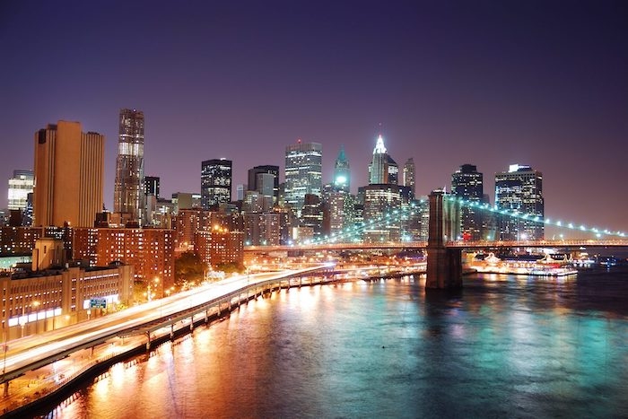 une photo de new york avec un pont des gratte ciels illuminées derriere un grand bouelvard