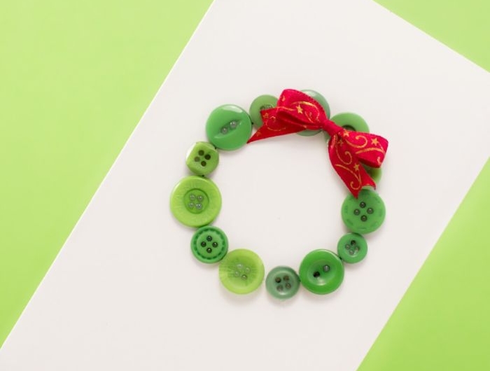 carte de noel fait main idée couronne de noel en boutons verts décorés de ruban rouge sur bout de papier blanc