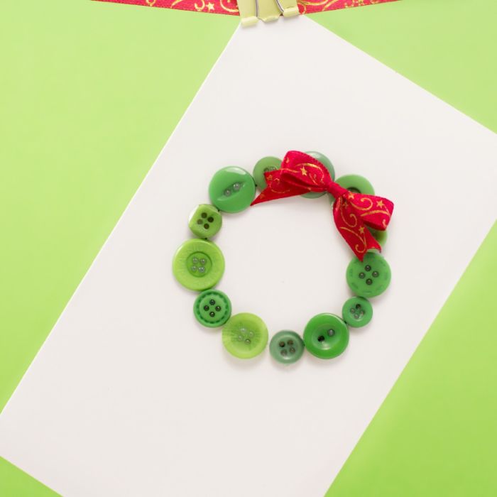 carte de noel fait main idée couronne de noel en boutons verts décorés de ruban rouge sur bout de papier blanc