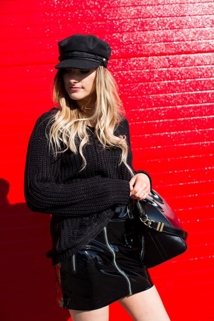 casquette tendance 2020 avec un jupe noir en cuire une fille blonde devant un mur rouge