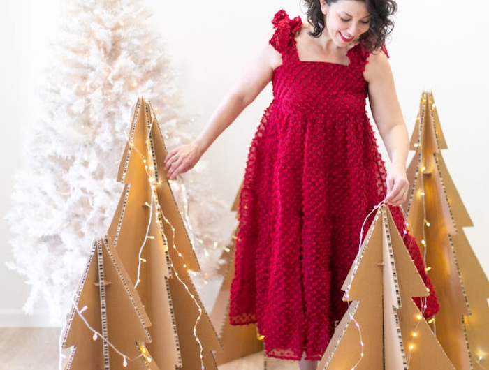 deco de noel fait main une femme en)robe rouge a cote des trois sapin)en carton avec des lumieres