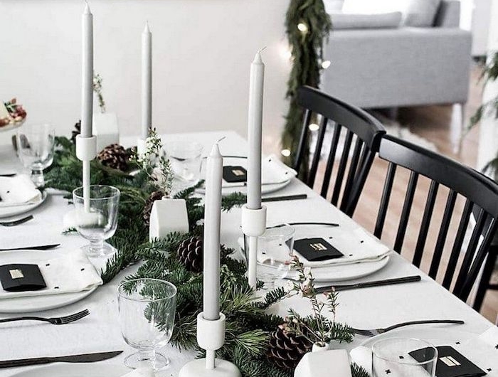deco de table noel avec des branches de sapin et des cones de pin une thématique en noir et blanc avec des bougies et des assiettes porcelaines