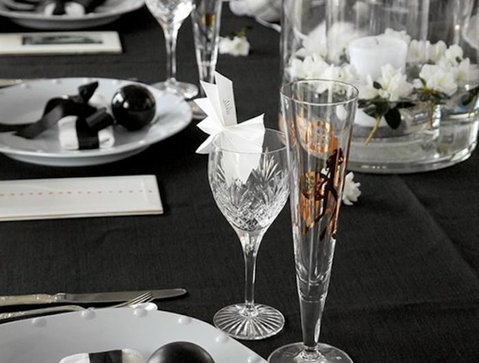 deco jou de l an en noir avec des assiettes blanches et verres cristalles un bouquet au milieu de la table