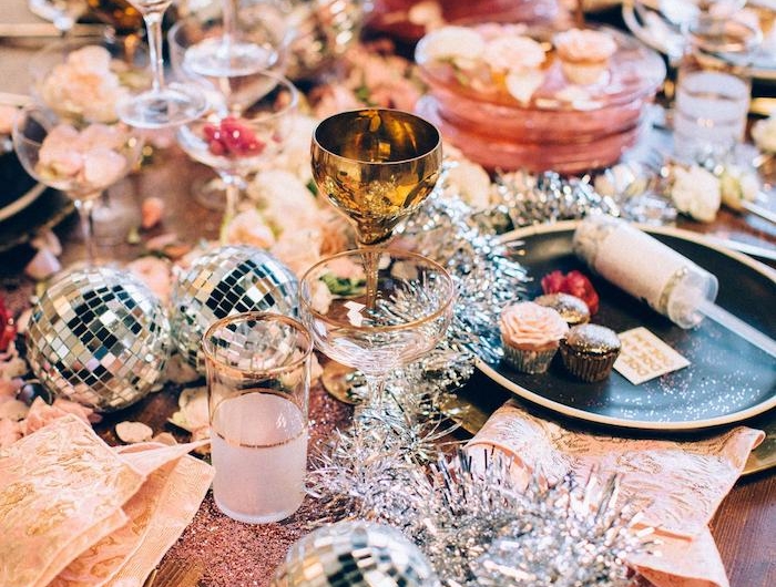 deco table reveillon st sylvestre avec des elements brillants et des balles disco des couverts et des verres dorres sur une table en bois