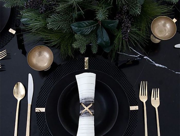 decoration de nouvel an sur une table noire avec des assiettes noires et couverts dores
