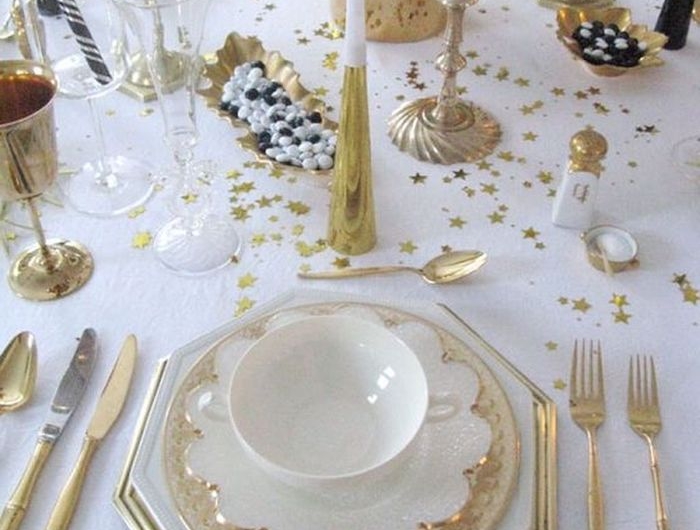 decoration table reveillon saint avec des asiettes blanches aux bordures dores des confettis parsemes sur une nappe blanche