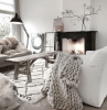 exemple de salon scandinave naturel avec table basse bois brut plaid grosses mailles sur canapé blanc tapis blanc fausse cheminée décorative noire
