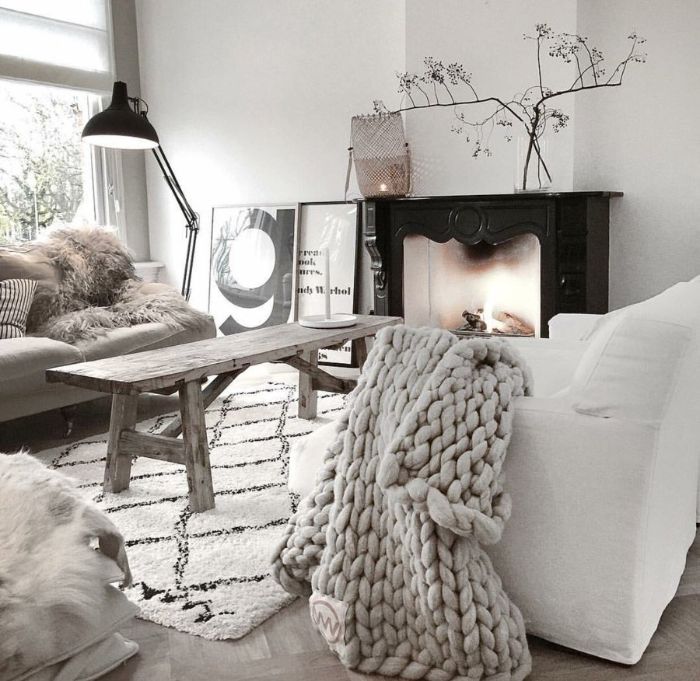 exemple de salon scandinave naturel avec table basse bois brut plaid grosses mailles sur canapé blanc tapis blanc fausse cheminée décorative noire