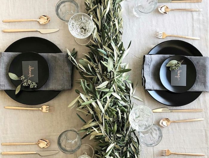 idee theme nouvel an avec un chemin de table a feuilles persistantes des couverts en or et des assiettes noirs avec des serviettes gris