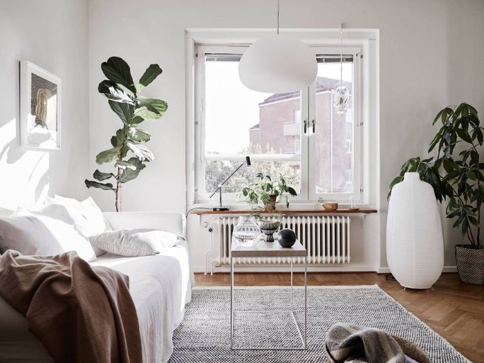 modele salon cocooning naturel avec canapé blanc plaid gris murs blancs tapis gris plantes vertes en pot