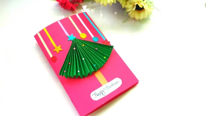 sapin de noel papier vert accordéon sur papier rose avec petites decorations et autres éléments décoratifs