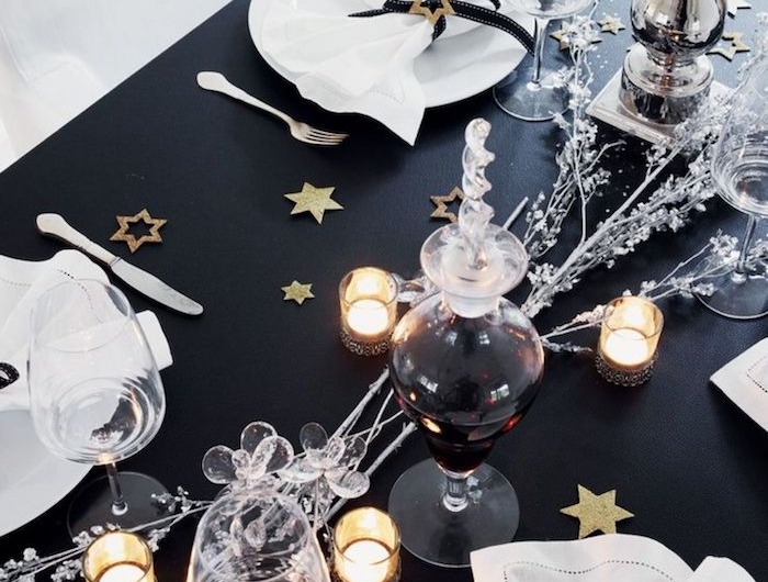 table de nouvel an en thematique noir avec des elements scintillantes comme des branches argentines et des etoiles decoratives dores