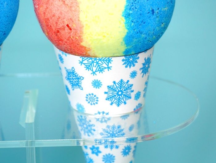 un cone de papier avec des flocons de neige qui tient une boule de bain multicolore