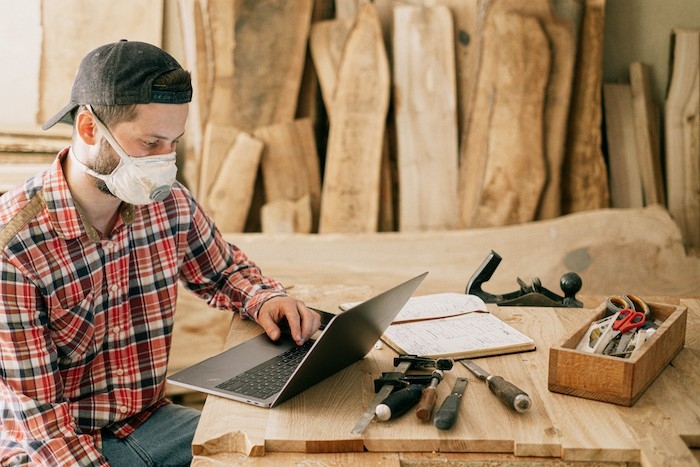 un homme avec masque et casquette devant l ordianteur pose sur une table rustique en bois