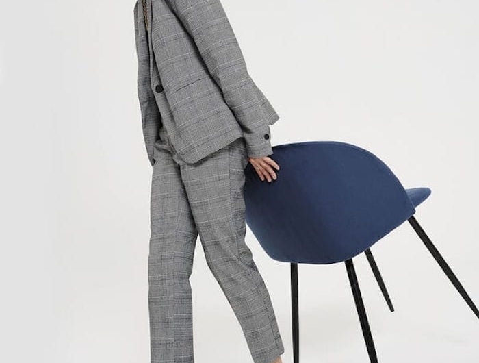 une femme dans un tailleur gris a carreau tient une chaise