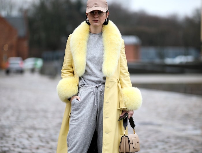 une femme vetue en costume de sport gris et un manteau jaune et casquette brun