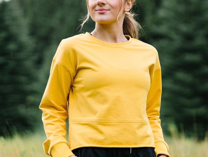 une fille dans la nature vetue en pantalon noir et une blouse jaune couleur tendance 2021