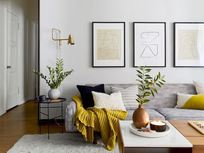 une salle de sejour avec un canape gris et une couette jaune des tableaux aux murs couleur tendance deco 2021