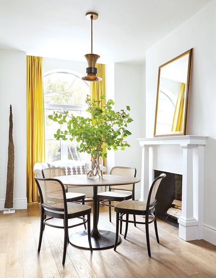 une salle de séjour avec une cheminee table avec quatre chaises et des rideaux jaunes couleur tendance deco 2021