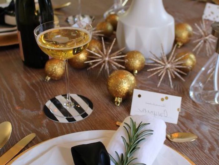 une table decore de reveillon avec es boules dores des branches de romarin et des tulips une bouteille de champagne a cote