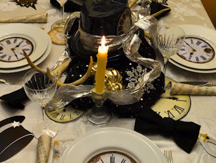 une table decoree pour le jour de l an avec un horologe dessine dans l assiette decorations au milieu de la table et des bougies allumees