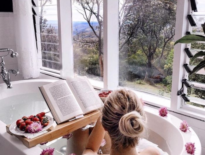 baignoire blanche avec belle vue sur l extérieur et decoration de fleurs pont de baignoire avec de fruits servis lecture livre