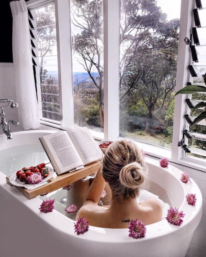baignoire blanche avec belle vue sur l extérieur et decoration de fleurs pont de baignoire avec de fruits servis lecture livre