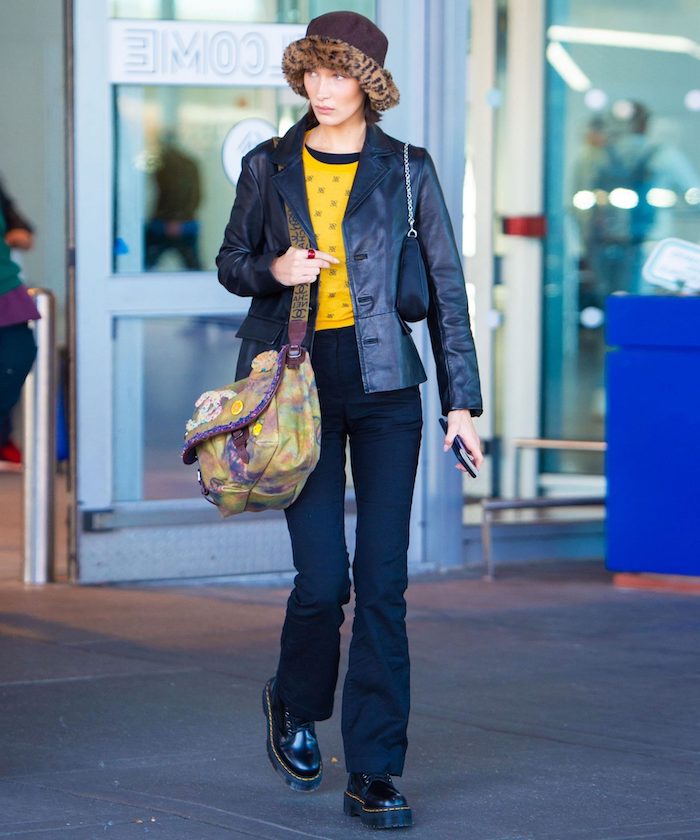 chaussure style doc martens bella hadid a l aeroport avec un chapeau fedora leopard et une blouse jaune