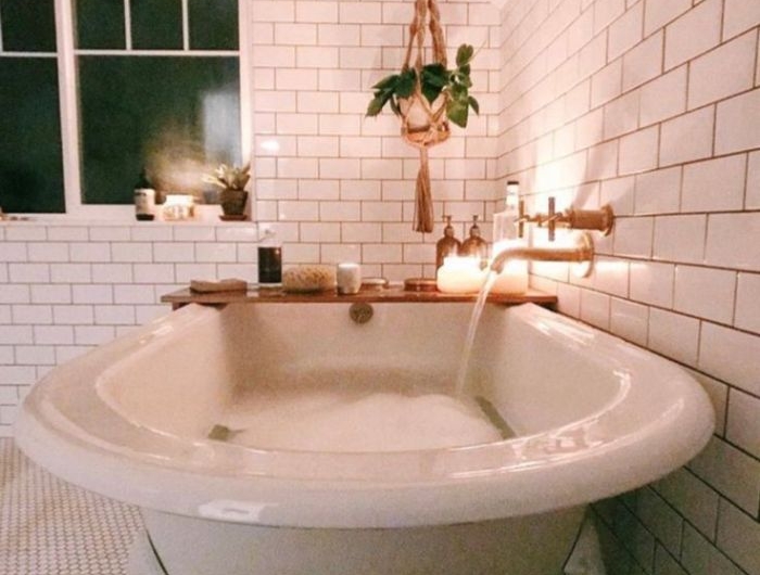 deco salle de bain blanche avec baignoire blanche et plantes suspendues macramé robinetterie en laiton bougies