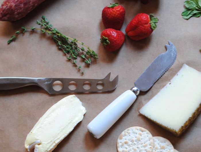 des couteaux de frommages et de beurre des fraises e raisins sur une table avec des herbes