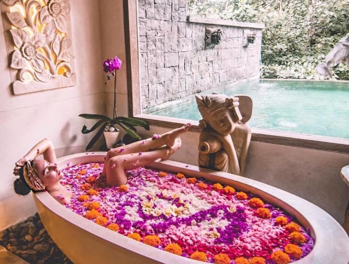 grande baignoire blanche remplie de pétales de fleurs avec vue sur l extérieur statuette de bouddha pierres d intérieur deco orientale cocooning