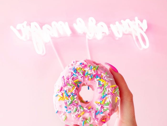 néon déco en blanc sur un mur rose derrière un main qui tien un beignet