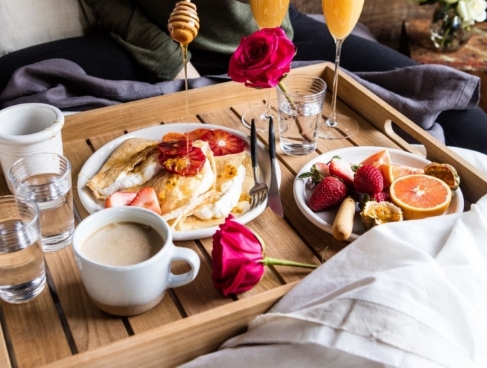 petit déjeuner au lit plateau bois tasse de café verre eau rose jus de fruits assiettes fruits