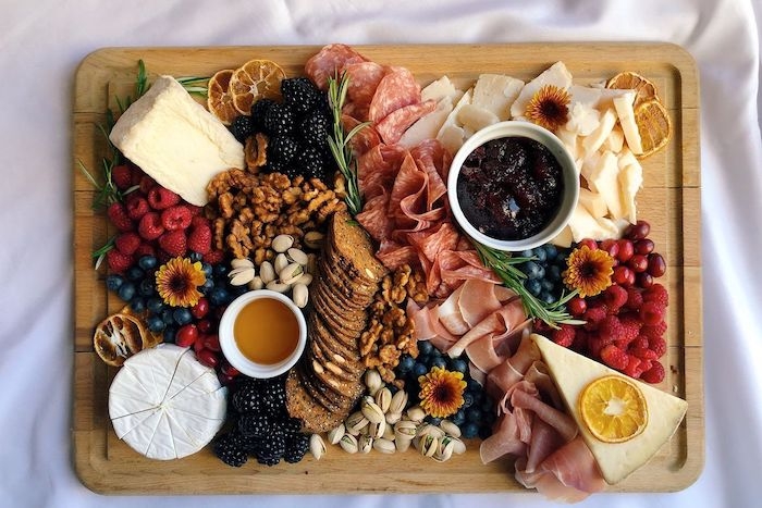 plateau charcuterie fromage moderne avec des fruits des noix et de la confiture garnis avec fleurs comestible