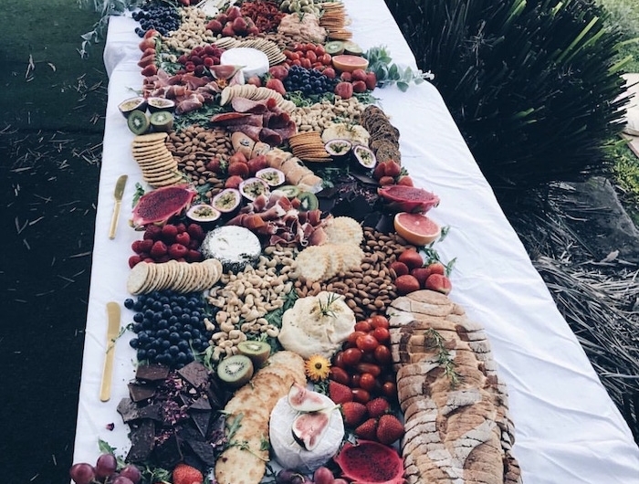 plateau charcuterie pour 10 personnes avec des fruis sur une nappe blanche dans un jardin