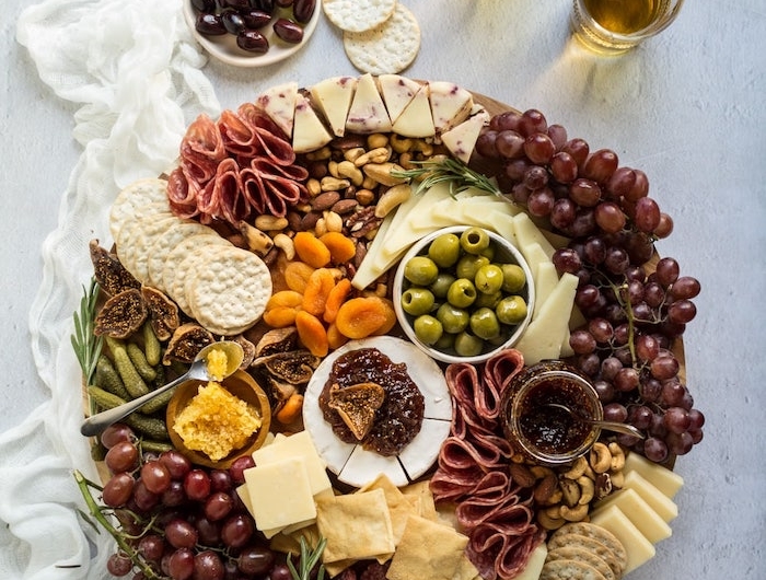 plnche apero ronde avec des raisin des fromages et des charcuteries avec de verrs de vin blanc