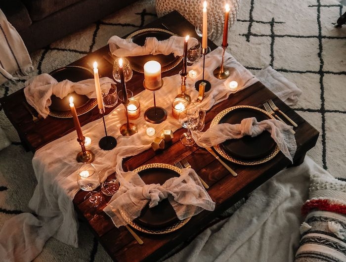 un diner servi sur un table basse en bois dans la salle de séjour avec un tapis blanc et des bougies allumés