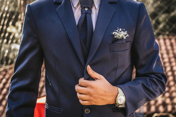 un homme vetu en costume bleu avec cravatte et montre autour de la poignée