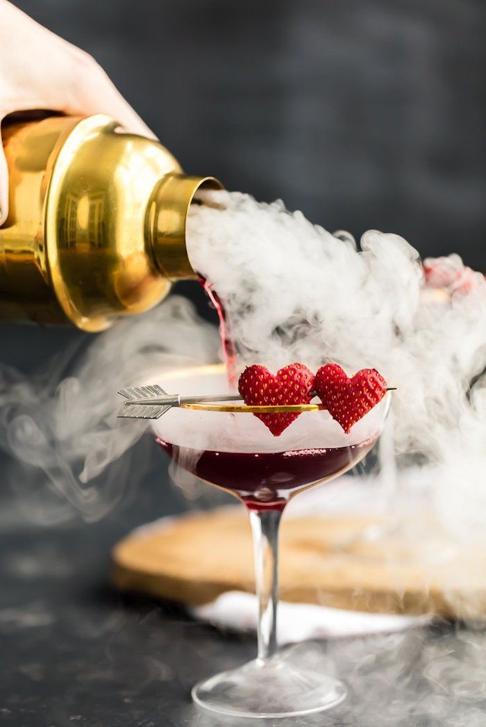 un main qui verse du cocktail dans un verre avec décore de fraises en forme de coeur