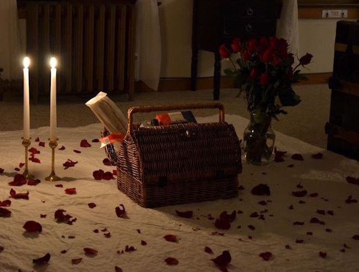 un panier de piquenique sur une couverture au sol avec une vase de roses et deux bougies