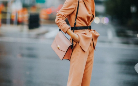 une femme avec des lunettes a soleil modernes un tailleur orange ceinture par la taille et sac en cuir de la meme cuuleur