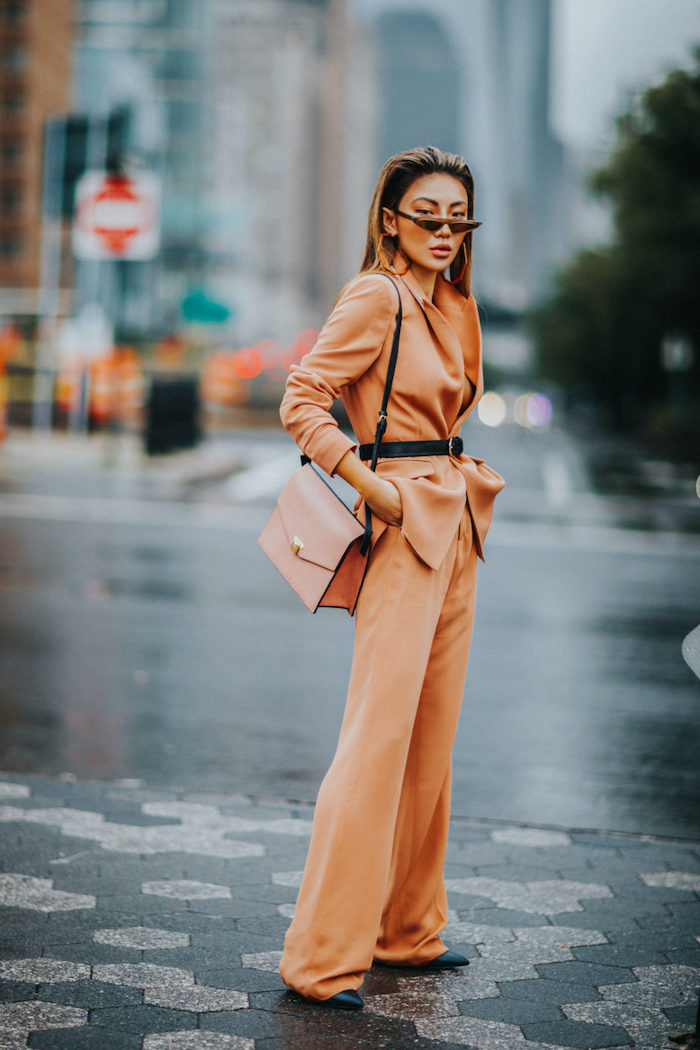 une femme avec des lunettes a soleil modernes un tailleur orange ceinture par la taille et sac en cuir de la meme cuuleur