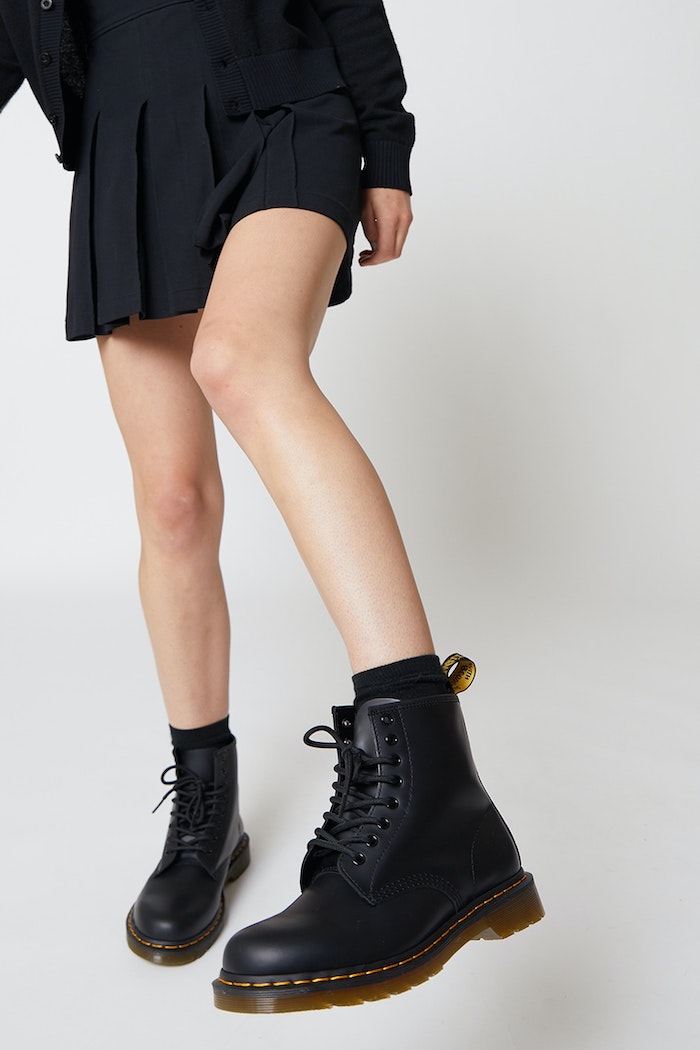 une femme en jupe plissée noire et des bottines doc martens