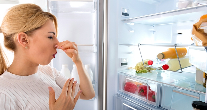 une femme qui se clot le nez devant un frigo ouvert marc de café contre les odeurs