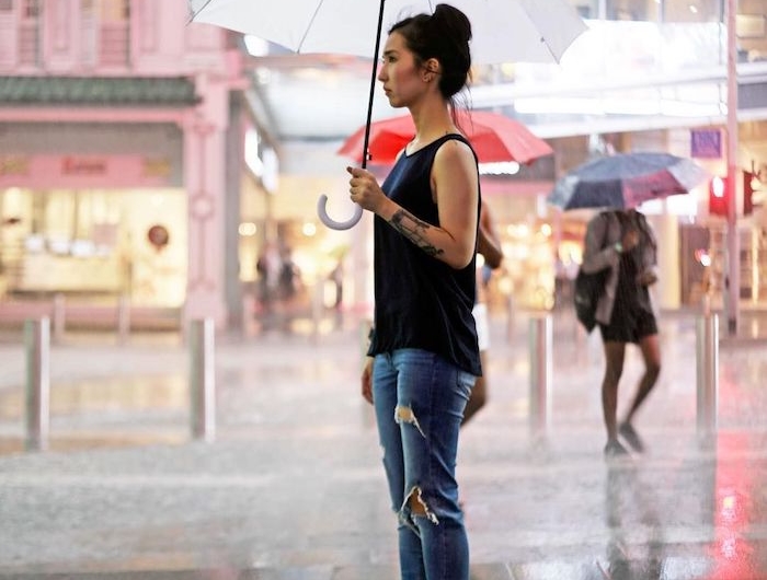 une femme qui tient une parapluie vetue en jean déchiré et top noir