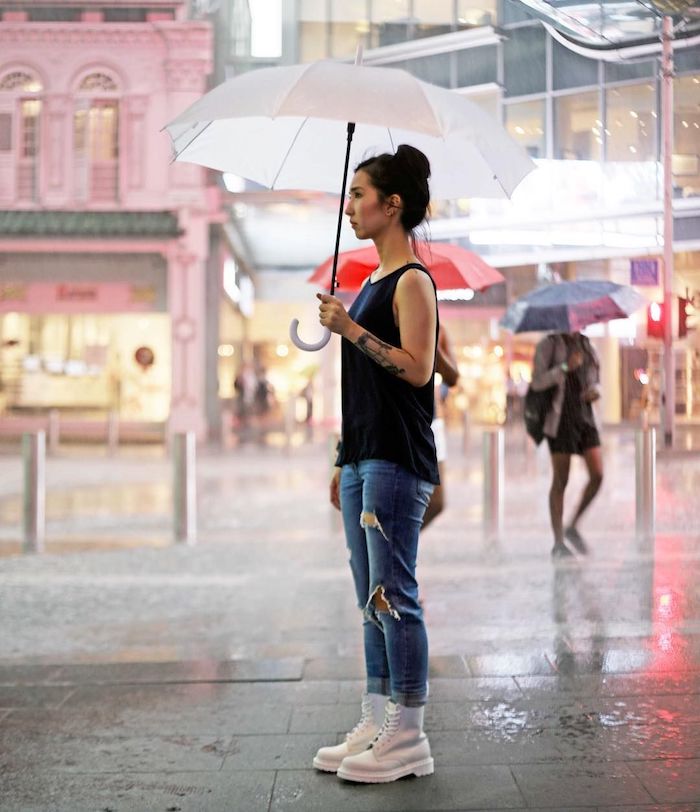 une femme qui tient une parapluie vetue en jean déchiré et top noir