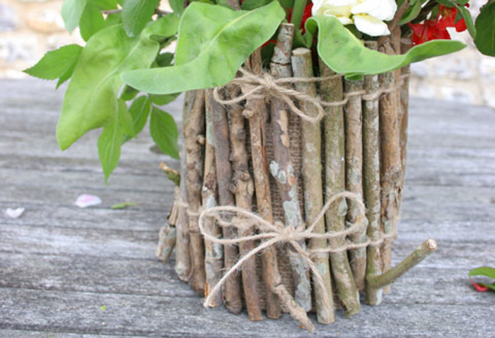 création avec pot de fleur élaboré avec des brindilles et ficelle et tissu de jute sur une surface en bois