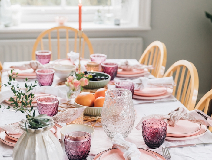 décoration saint valentin avec des assiettes et verres roses une bougie rouge allumée et es oranges