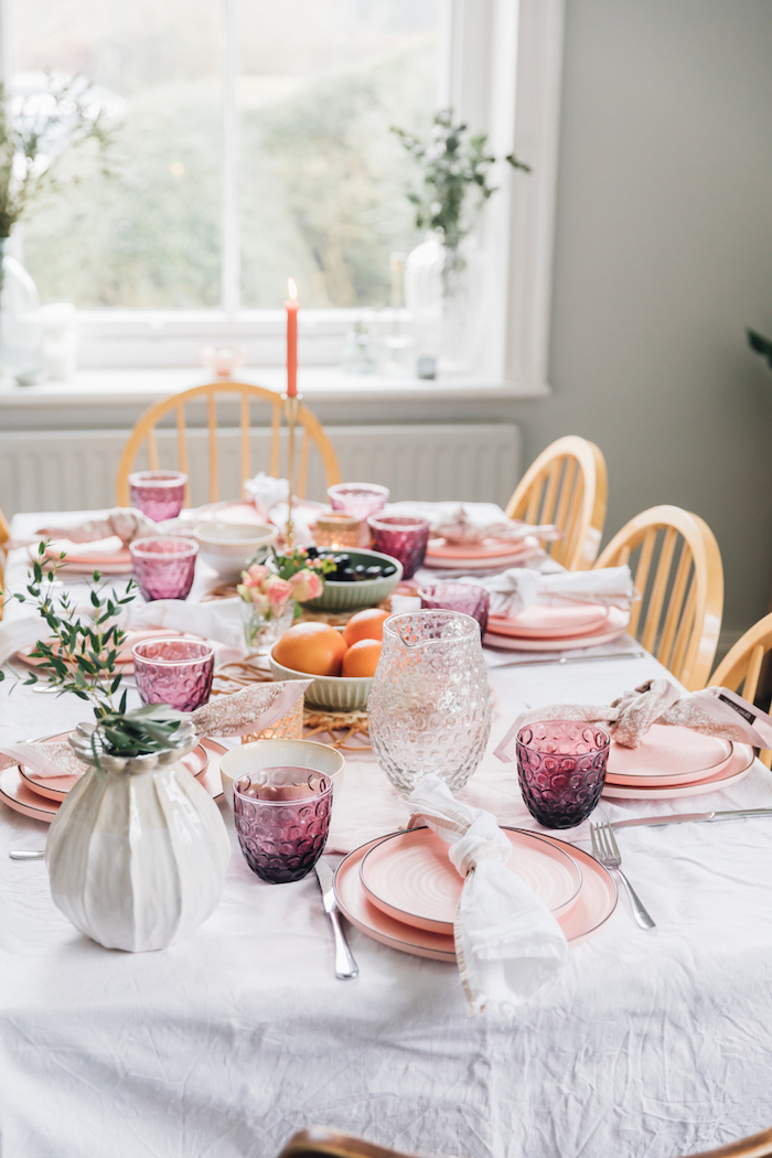décoration saint valentin avec des assiettes et verres roses une bougie rouge allumée et es oranges